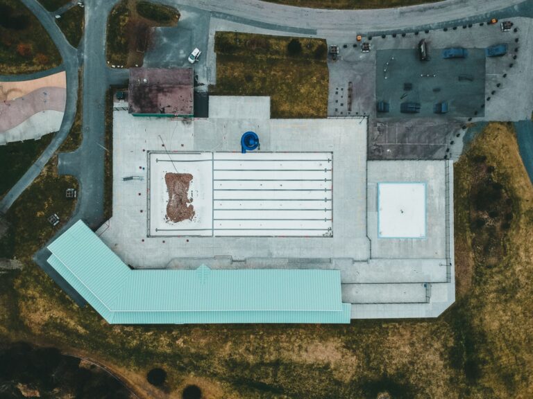 Aerial shot of a large building with a flat concrete rooftop and surrounding grassy area.